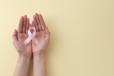 Woman with pink awareness ribbon on pale yellow background, top view. Space for text