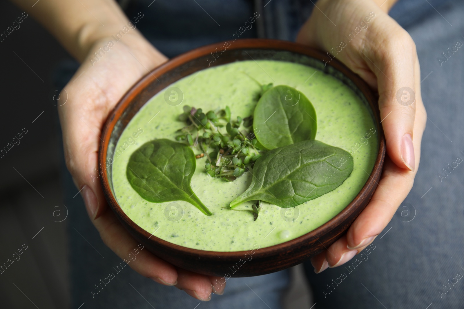 Photo of Woman holding bowl of delicious spinach cream soup, closeup