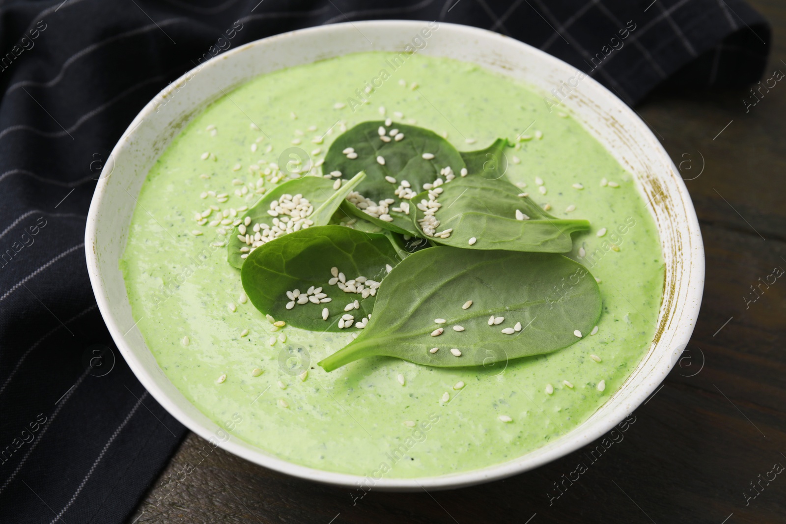 Photo of Delicious spinach cream soup with fresh leaves and sesame seeds in bowl on wooden table