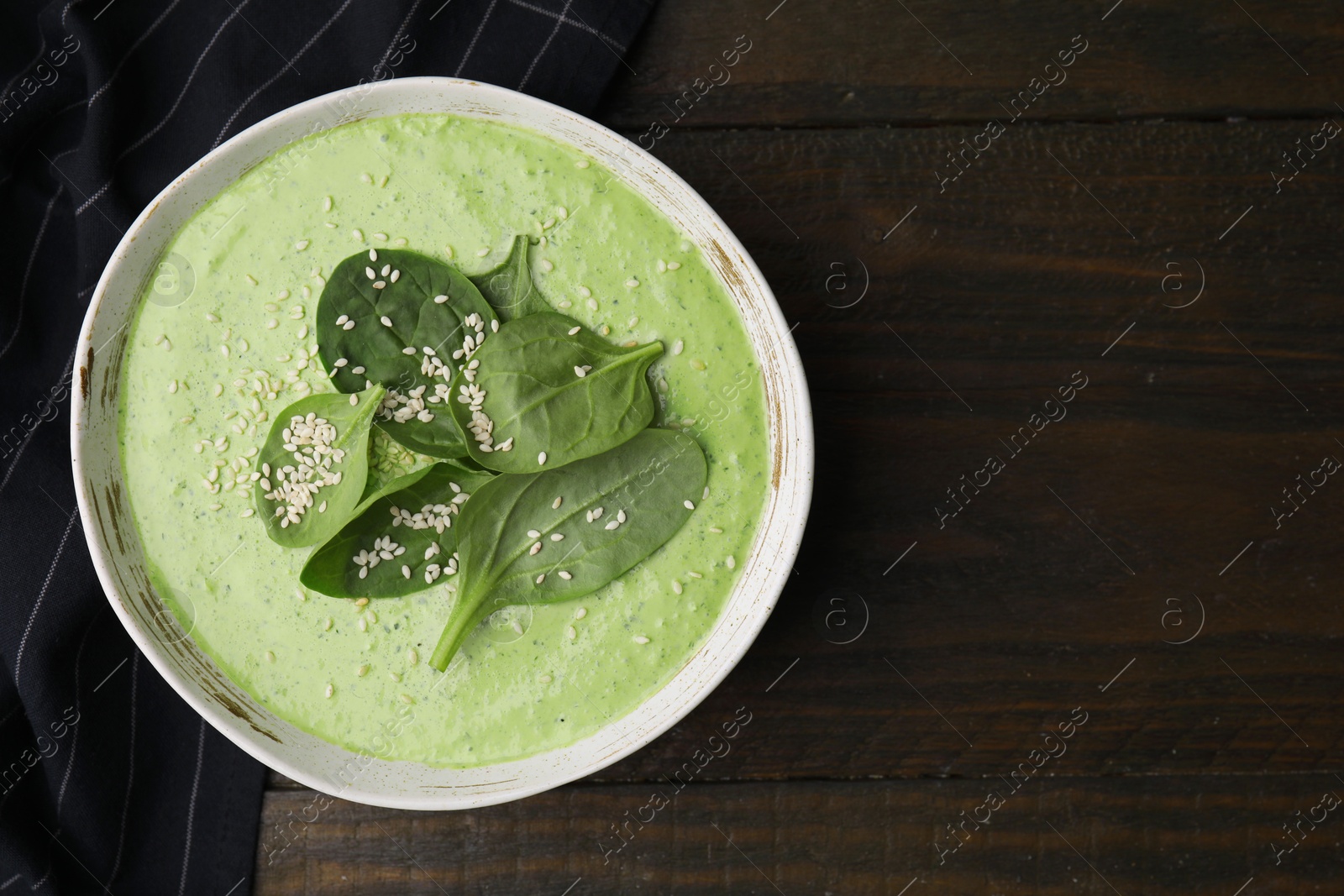 Photo of Delicious spinach cream soup with fresh leaves and sesame seeds in bowl on wooden table, top view. Space for text