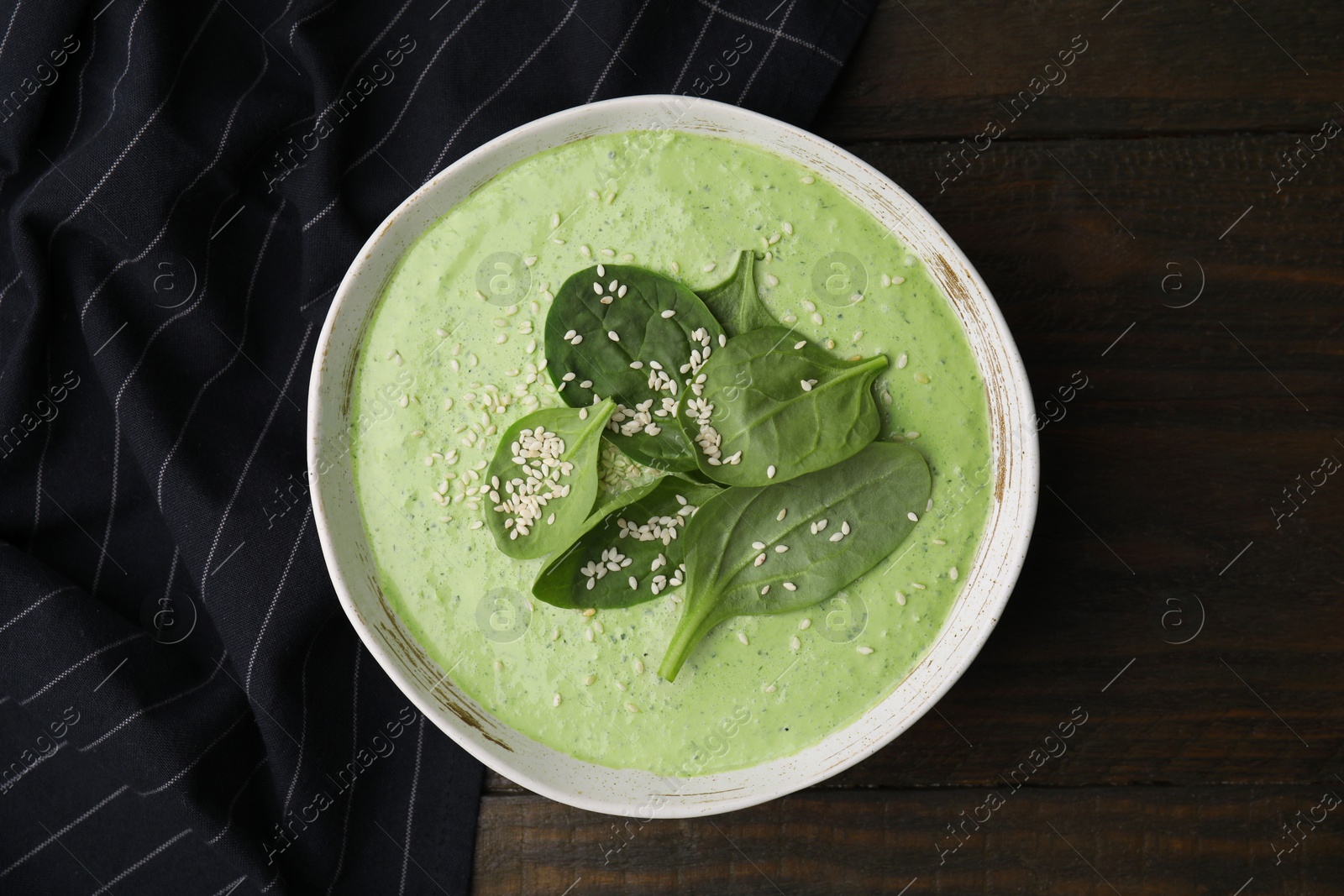 Photo of Delicious spinach cream soup with fresh leaves and sesame seeds in bowl on wooden table, top view