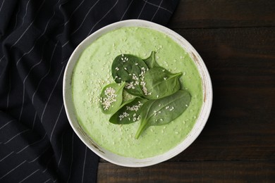 Photo of Delicious spinach cream soup with fresh leaves and sesame seeds in bowl on wooden table, top view