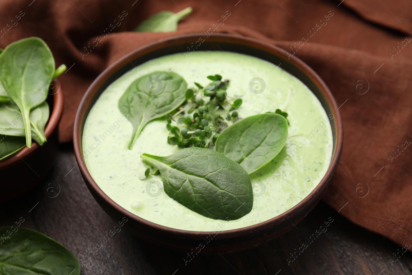 Photo of Delicious spinach cream soup with fresh leaves and microgreens in bowl on wooden table