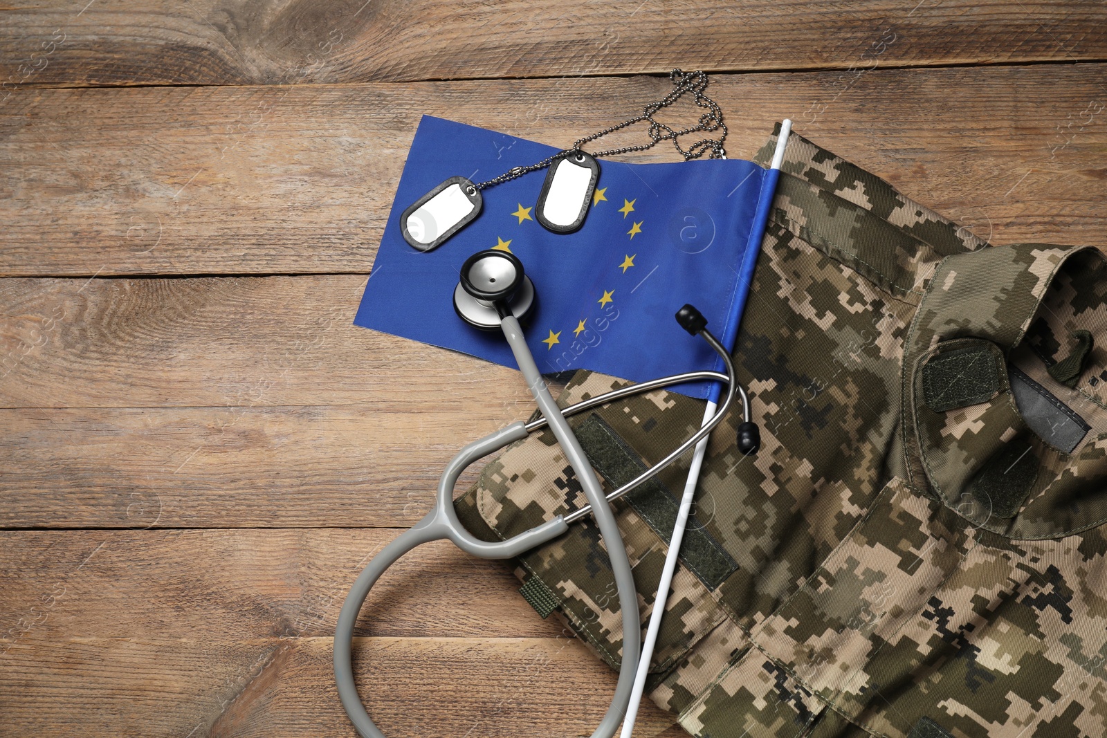 Photo of Stethoscope, flag of European Union, tags and military uniform on wooden table, flat lay. Space for text