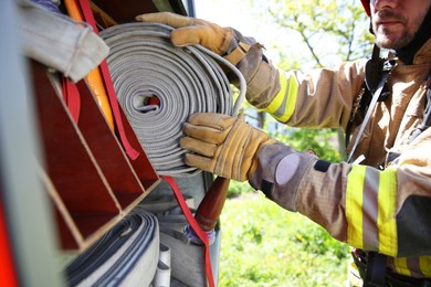 Firefighter in uniform with fire hose near truck outdoors, closeup