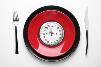 Plates with analog weighing scale display and cutlery isolated on white, top view