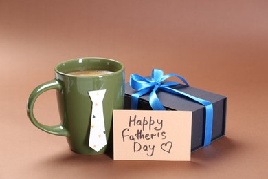 Photo of Card with phrase Happy Father's Day, coffee and gift on brown background