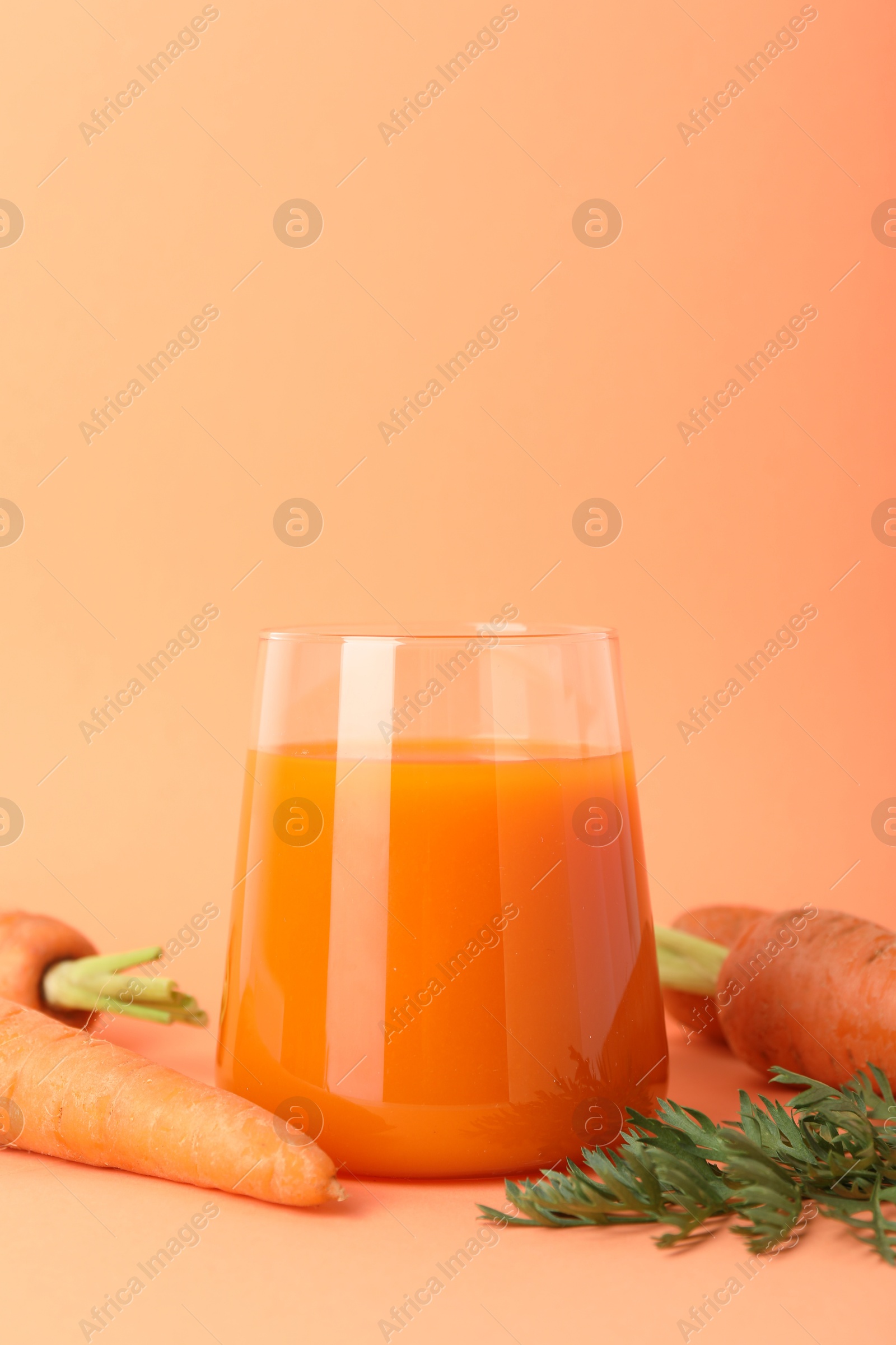 Photo of Fresh carrot juice in glass and vegetables on coral background