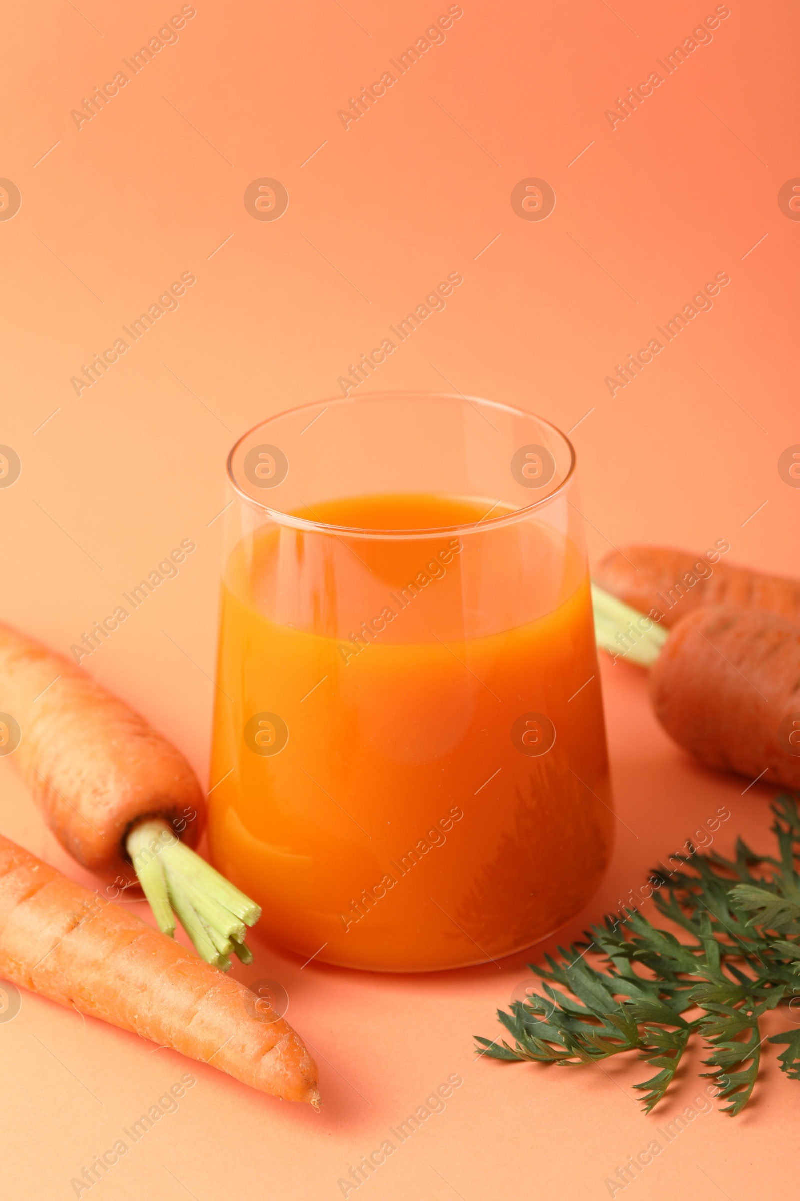 Photo of Fresh carrot juice in glass and vegetables on coral background