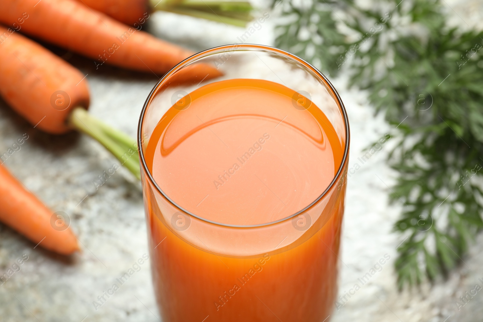 Photo of Fresh carrot juice in glass and vegetables on grey table, closeup