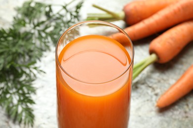 Photo of Fresh carrot juice in glass and vegetables on grey table, closeup