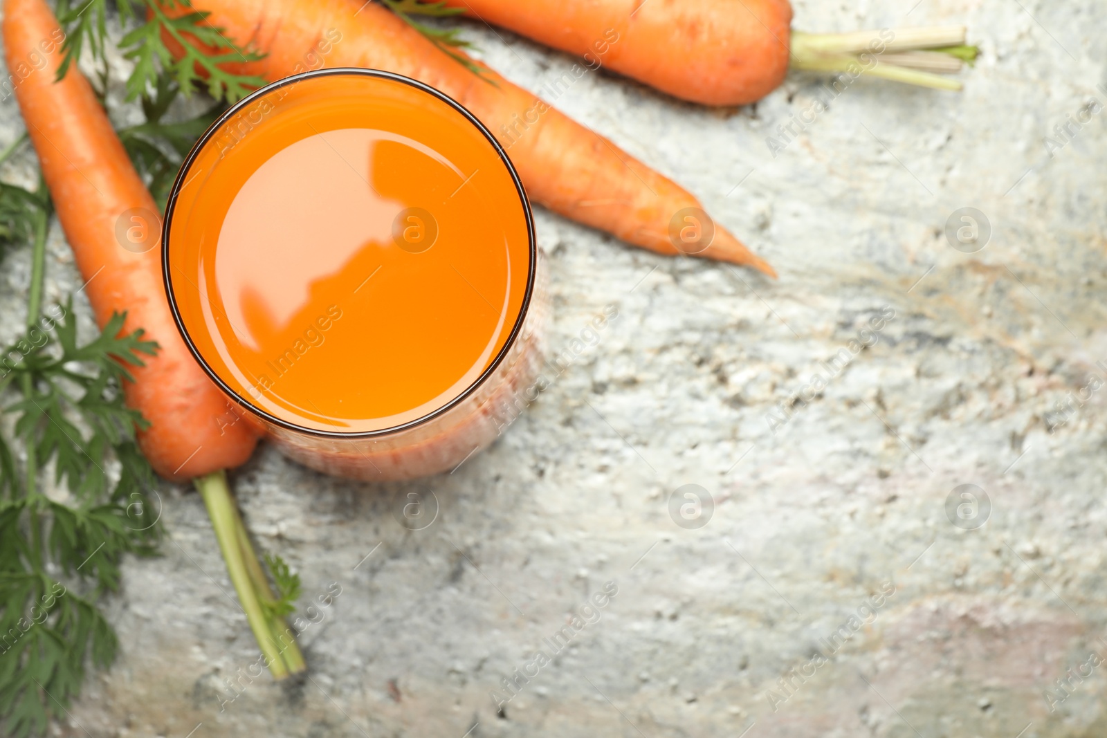 Photo of Fresh carrot juice in glass and vegetables on grey textured table, above view. Space for text