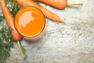 Photo of Fresh carrot juice in glass and vegetables on grey textured table, above view. Space for text