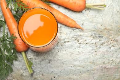 Fresh carrot juice in glass and vegetables on grey textured table, above view. Space for text