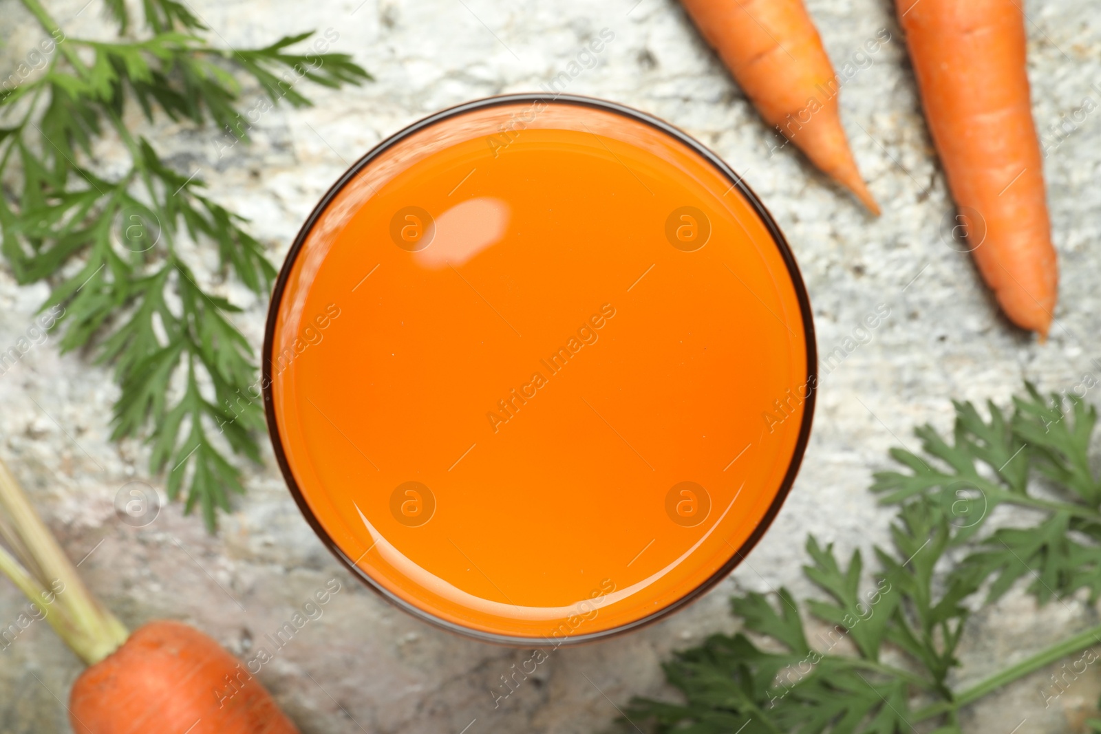 Photo of Fresh carrot juice in glass and vegetables on grey textured table, flat lay