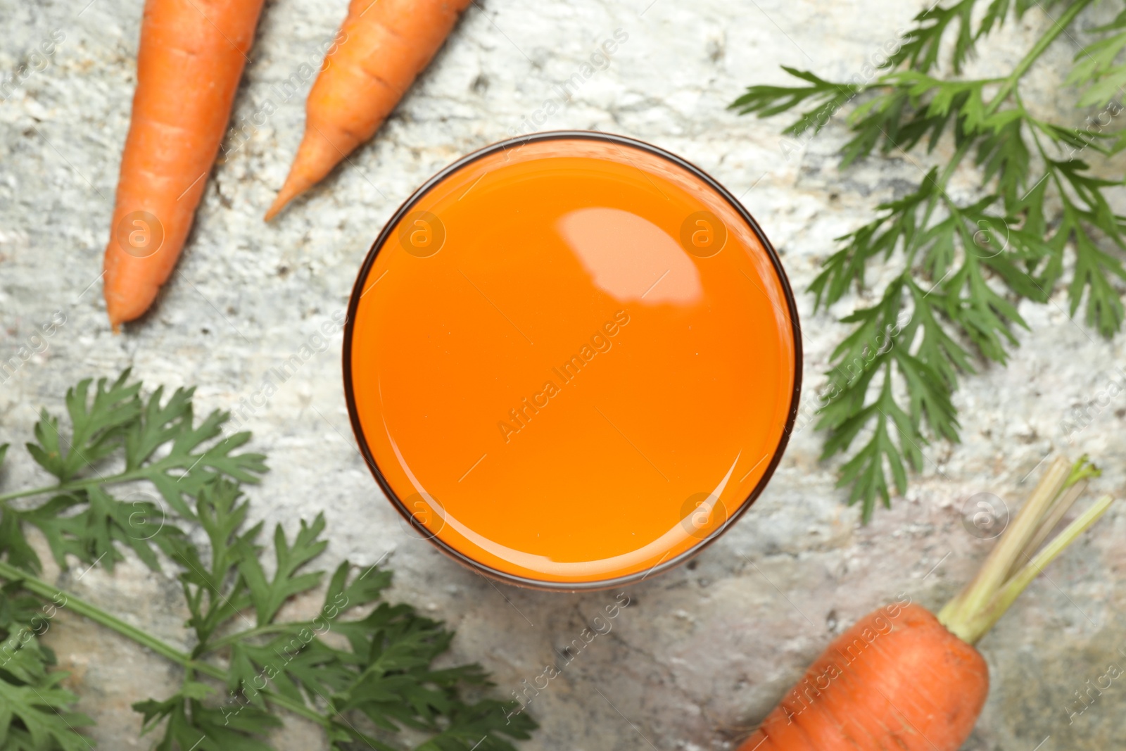 Photo of Fresh carrot juice in glass and vegetables on grey textured table, flat lay