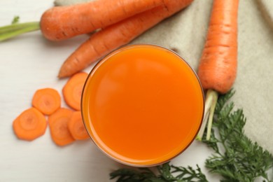 Fresh carrot juice in glass and vegetables on light table, flat lay