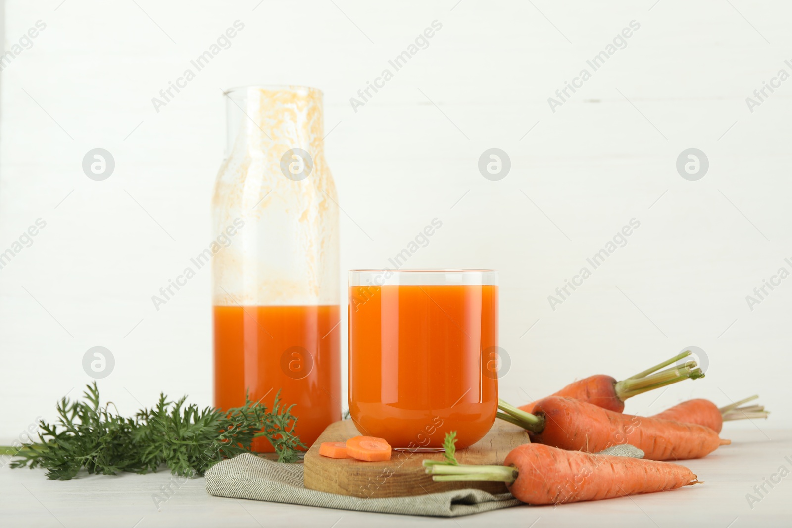 Photo of Fresh carrot juice and vegetables on light table