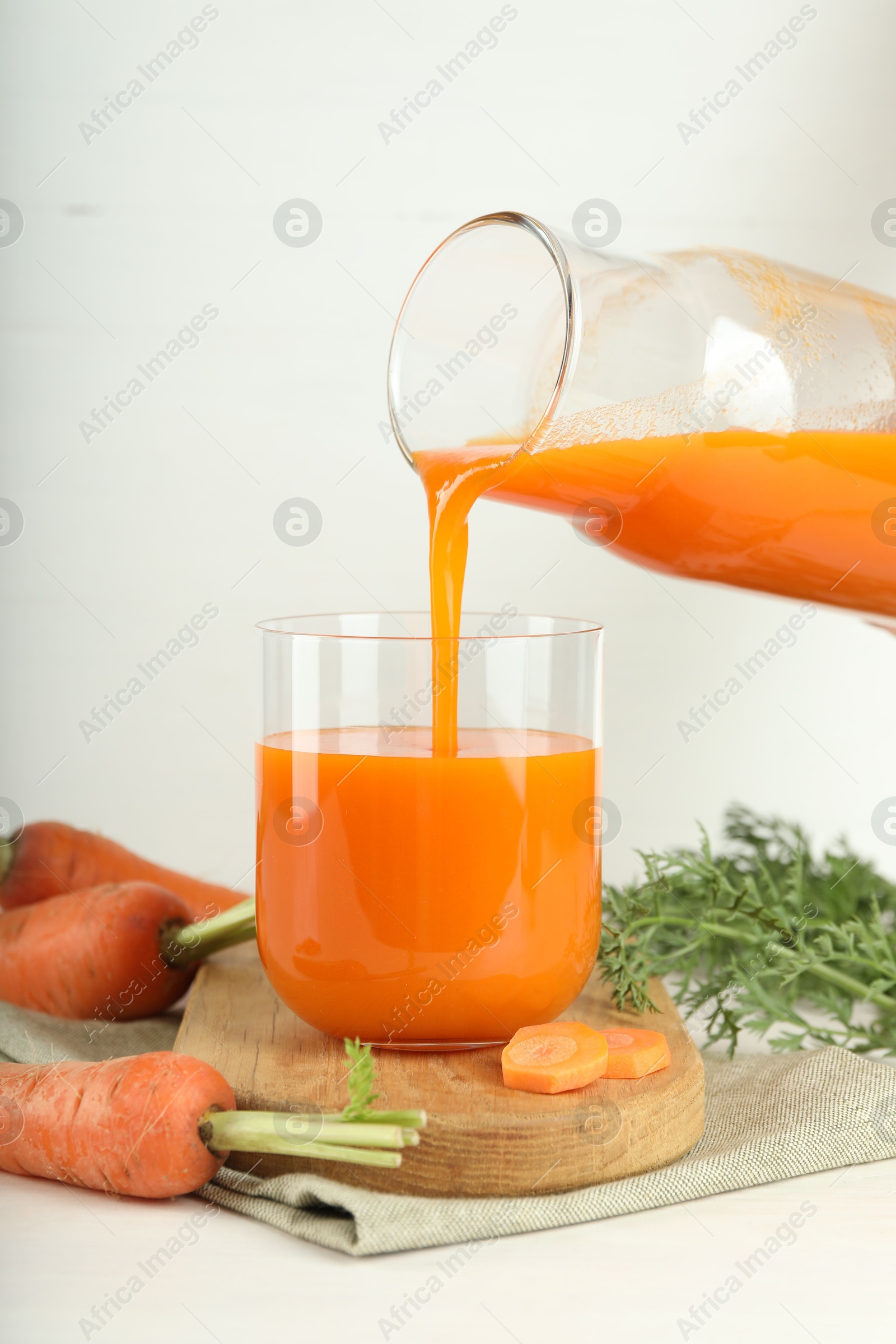 Photo of Pouring fresh carrot juice from bottle into glass at light table, closeup