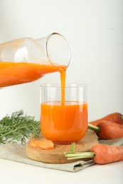 Photo of Pouring fresh carrot juice from bottle into glass at light table, closeup