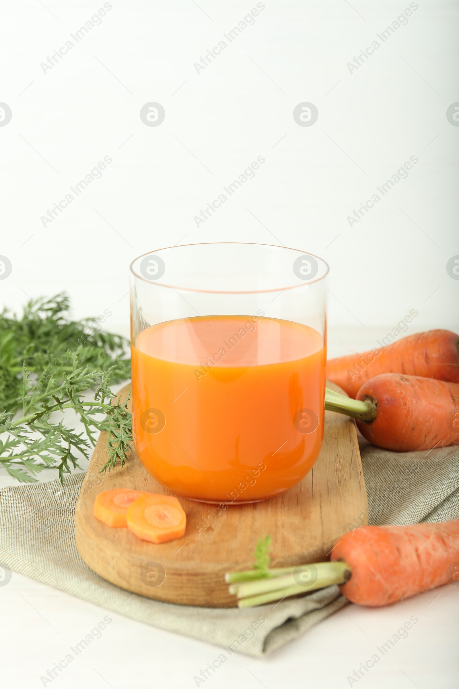 Photo of Fresh carrot juice in glass and vegetables on light table