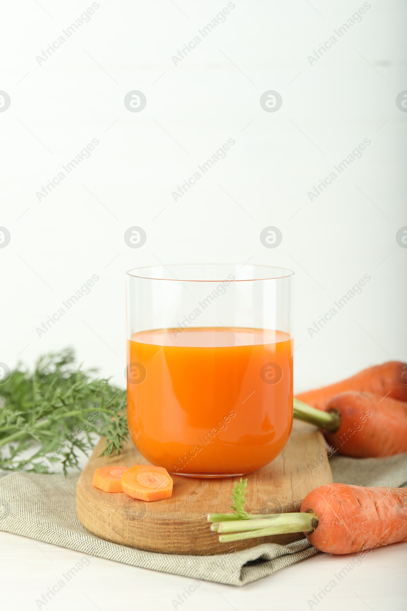 Photo of Fresh carrot juice in glass and vegetables on light table