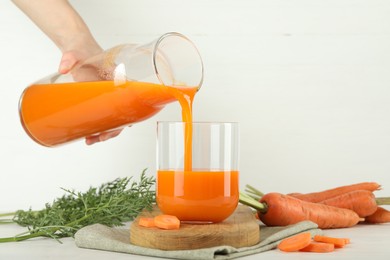 Photo of Woman pouring fresh carrot juice from bottle into glass at light table, closeup
