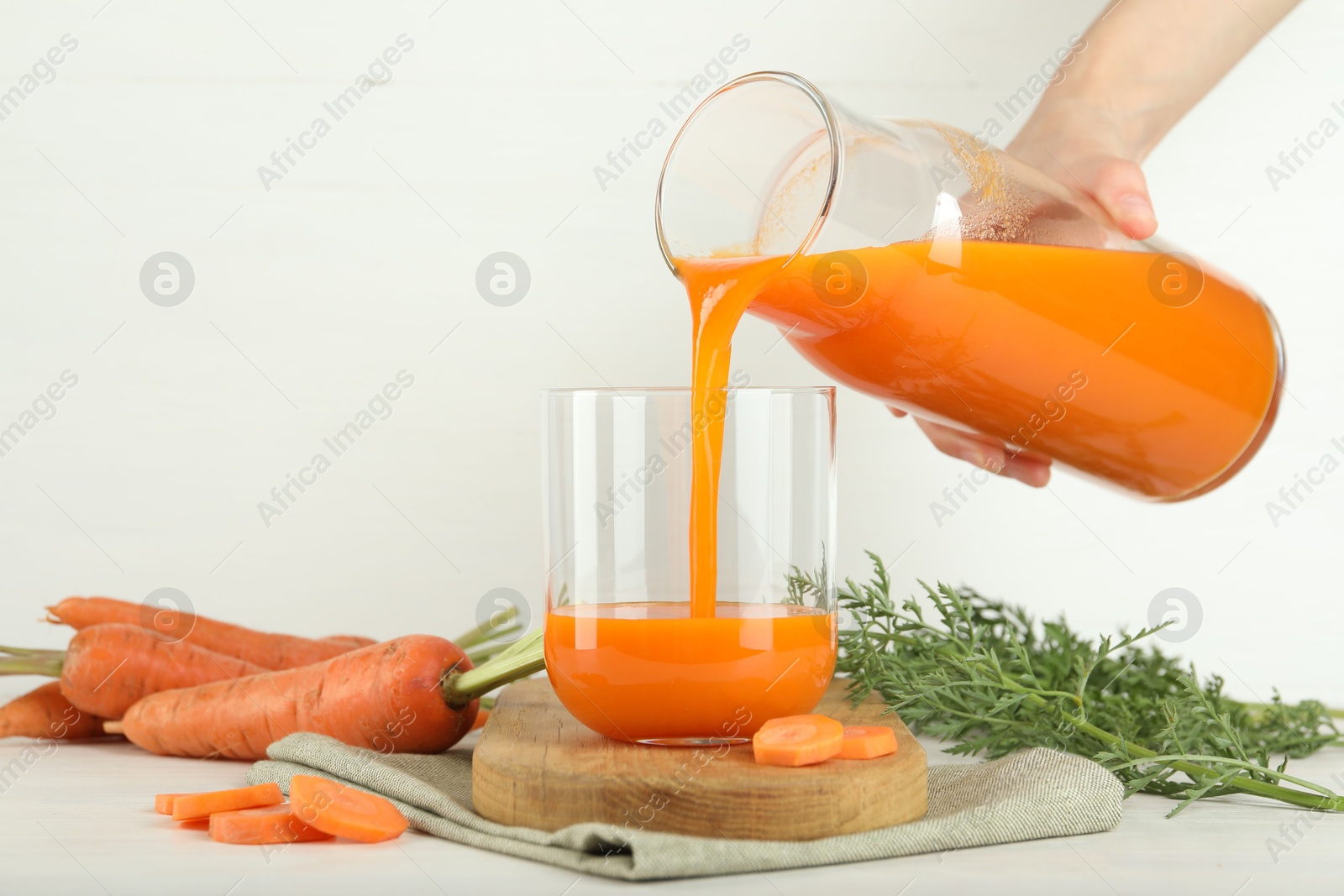 Photo of Woman pouring fresh carrot juice from bottle into glass at light table, closeup