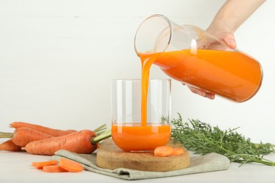 Photo of Woman pouring fresh carrot juice from bottle into glass at light table, closeup