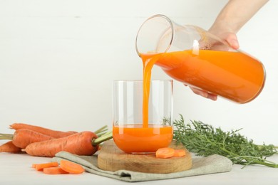 Woman pouring fresh carrot juice from bottle into glass at light table, closeup