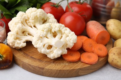 Photo of Cooking tasty stew. Cauliflower, tomatoes, carrot and potatoes on light grey table