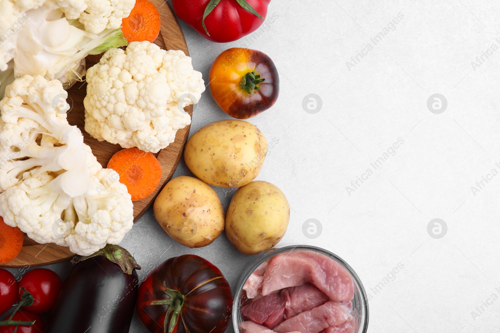 Photo of Different vegetables and raw meat for stew on light grey table, top view. Space for text