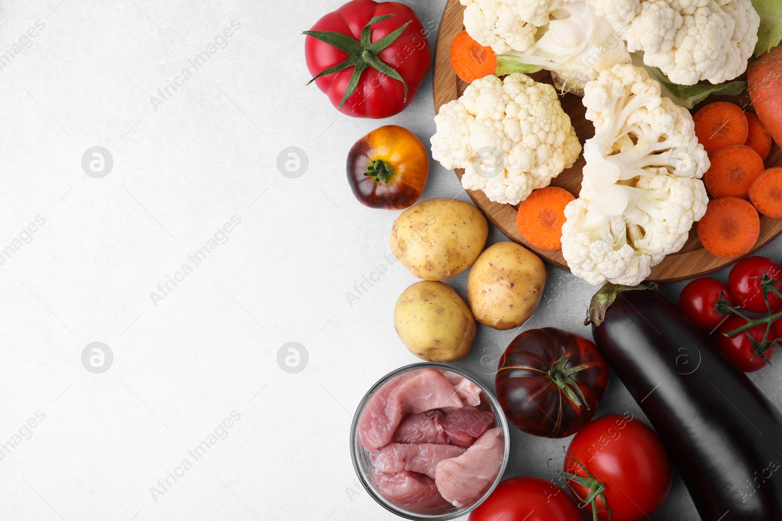 Photo of Different vegetables and raw meat for stew on light grey table, top view. Space for text