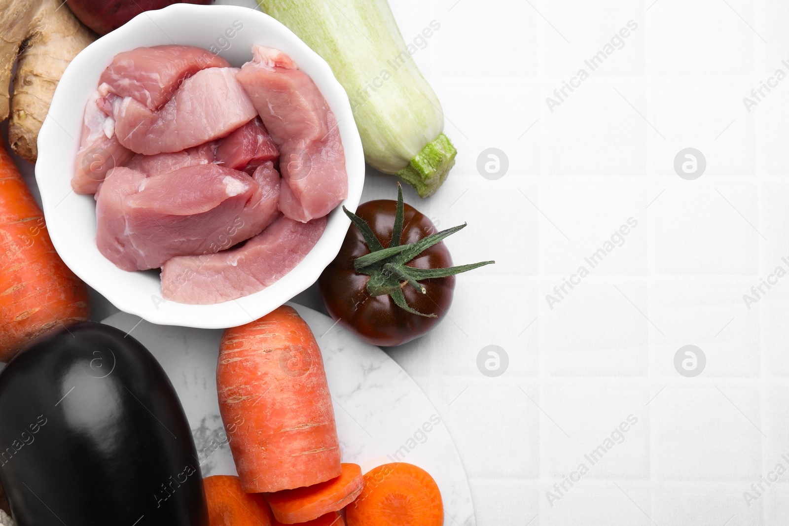 Photo of Different vegetables and raw meat for stew on white tiled table, top view. Space for text