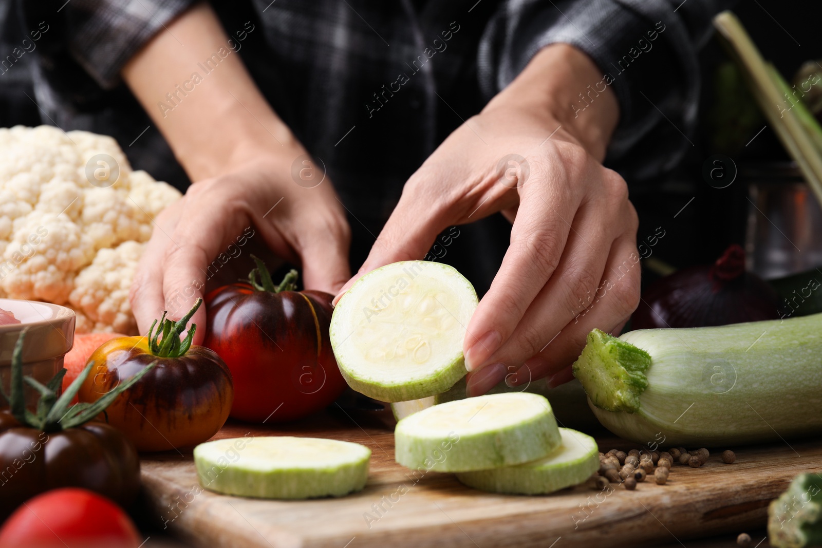 Photo of Cooking vegetable stew. Woman with cut zucchini and tomato at table, closeup