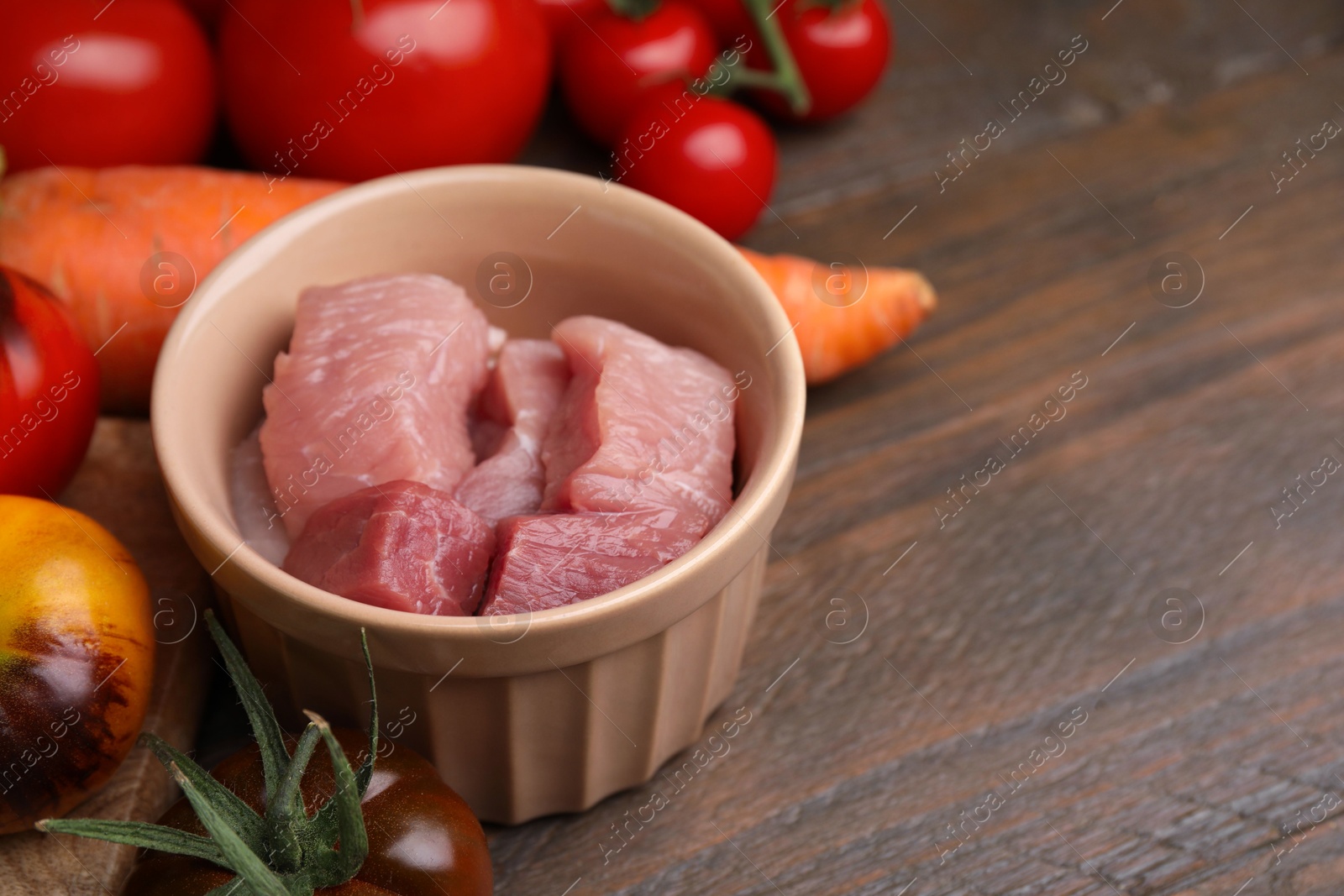 Photo of Cooking tasty stew. Raw meat, tomatoes and carrot on wooden table, space for text