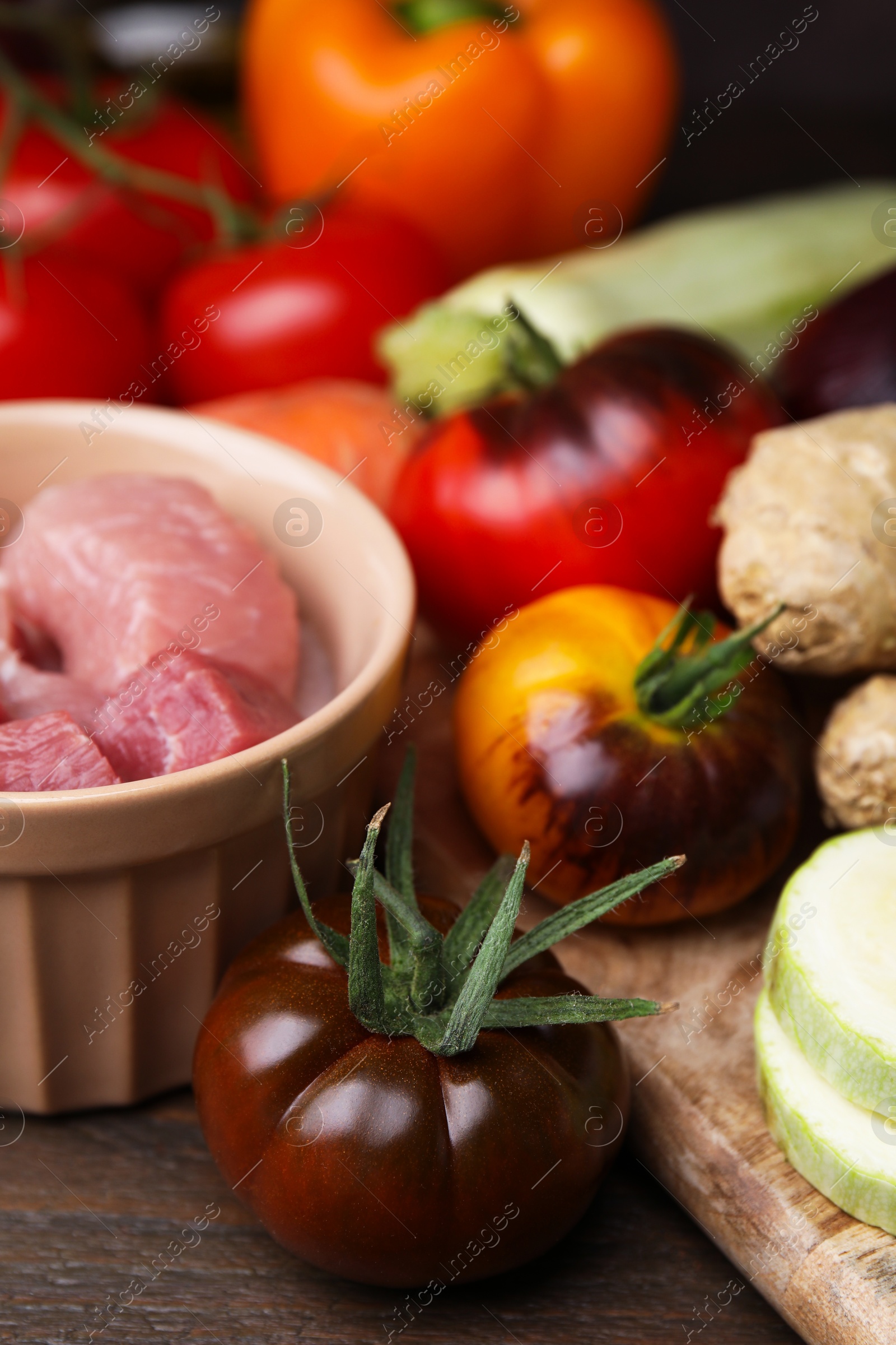 Photo of Cooking tasty stew. Fresh tomatoes and raw meat on wooden table