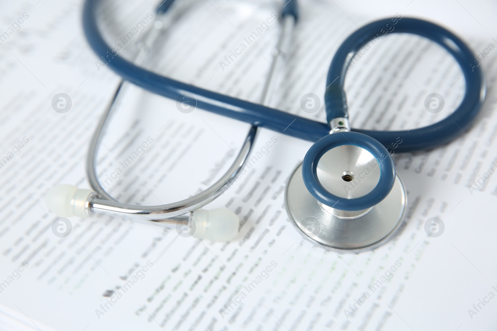 Photo of One medical stethoscope and book on table, closeup