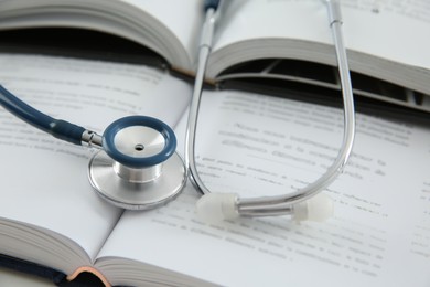 Photo of One medical stethoscope and books on table, closeup