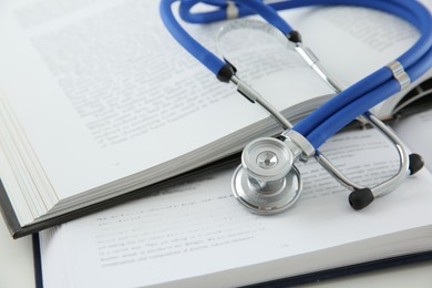 Photo of One medical stethoscope and books on white table, closeup