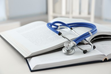 One medical stethoscope and books on white table, closeup