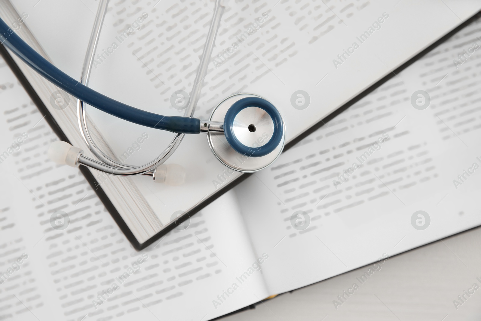 Photo of One new medical stethoscope and books on white wooden table, top view