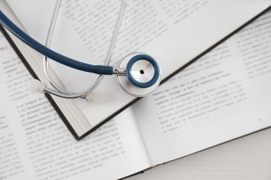Photo of One new medical stethoscope and books on white wooden table, top view