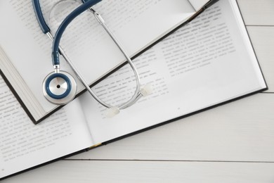 Photo of One new medical stethoscope and books on white wooden table, top view