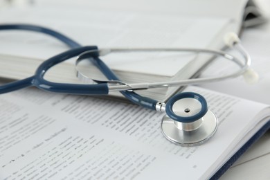 Photo of One new medical stethoscope and books on white wooden table, closeup