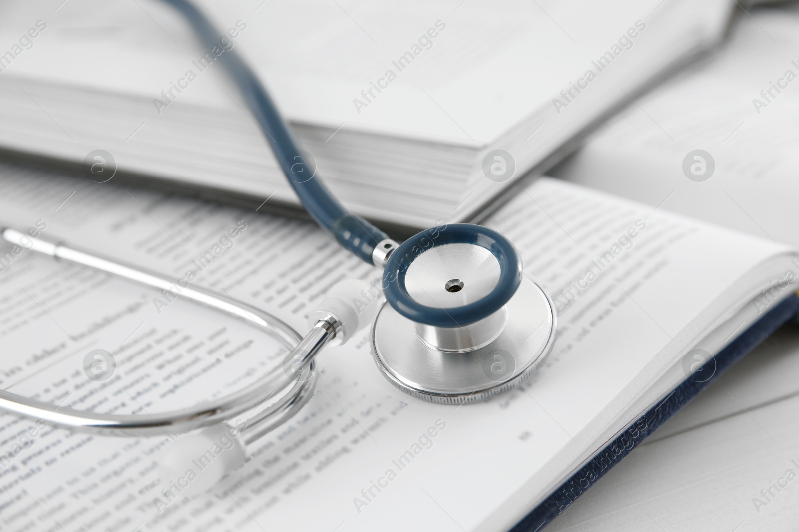 Photo of One new medical stethoscope and books on white wooden table, closeup