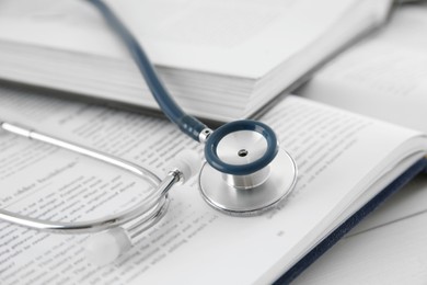 One new medical stethoscope and books on white wooden table, closeup