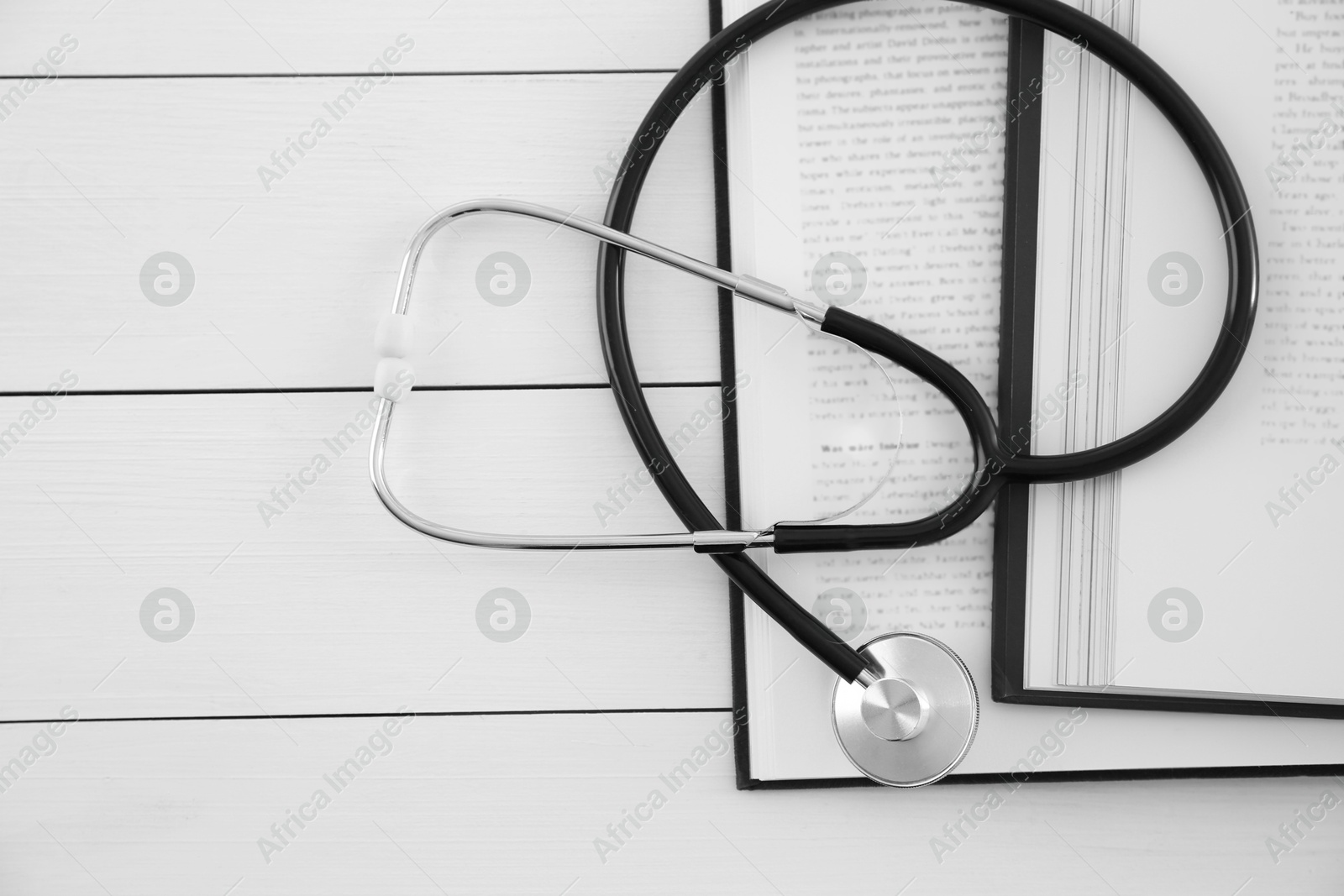 Photo of One new medical stethoscope and books on white wooden table, top view. Space for text