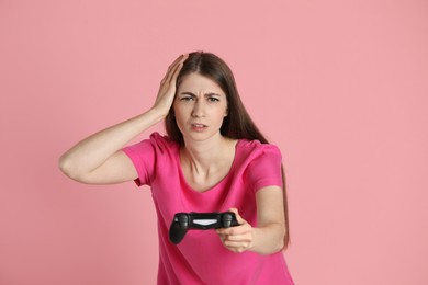 Unhappy woman playing video games with controller on pink background