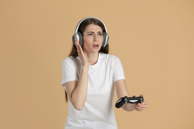 Woman in headphones playing video games with controller on beige background